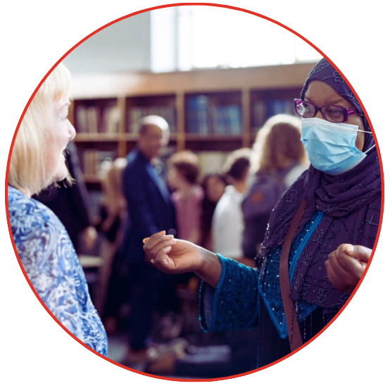 Two women wearing face masks while reading in a library, surrounded by books and a quiet study atmosphere.