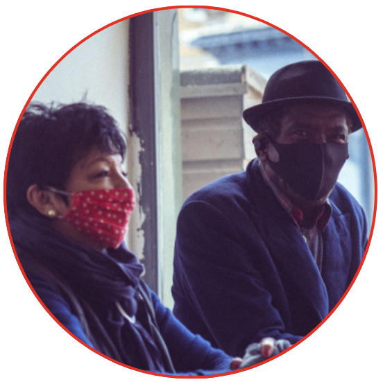 Two individuals in face masks seated on a bench, maintaining social distance in a public space.