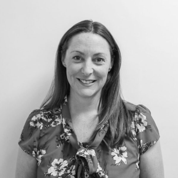 A woman wearing a floral shirt stands confidently in front of a clean white wall, showcasing her vibrant style.