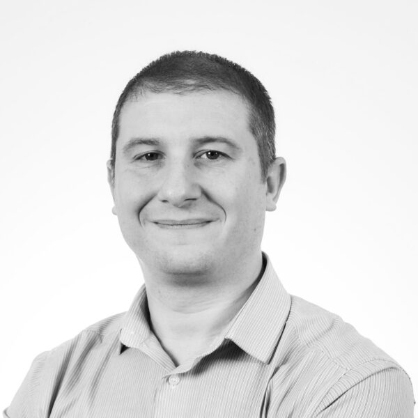 A cheerful man wearing a shirt smiles at the camera, radiating positivity and friendliness.