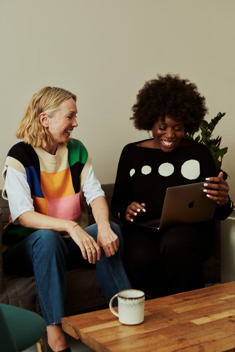 Two women relax together on a cozy couch, enjoying each other's company and sharing a lighthearted moment.